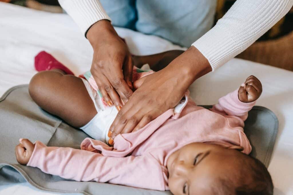 Pampers Swaddlers vs Cruisers: Which One is the Best Diaper for Your Little One? 4 Hands with brown skin changing diaper of a brown skin baby for article about Pampers Swaddlers vs Cruisers