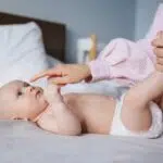 photo of baby on a bed wearing a diaper and an adult arm booping its nose for post about seventh generation diapers reviews