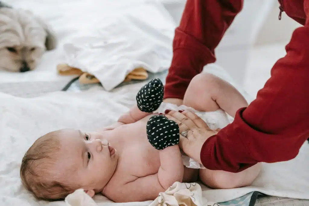 image of a baby with black mittens and adult hands on diaper about to change diaper for blog post huggies special delivery vs pampers pure